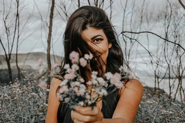 mulher segurando buque de flores em floresta de arvores sem folhas