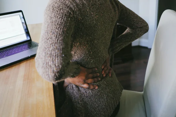 Foto de uma mulher negra de costas com a mão na lombar sentindo dor no nervo ciático - Metrópoles