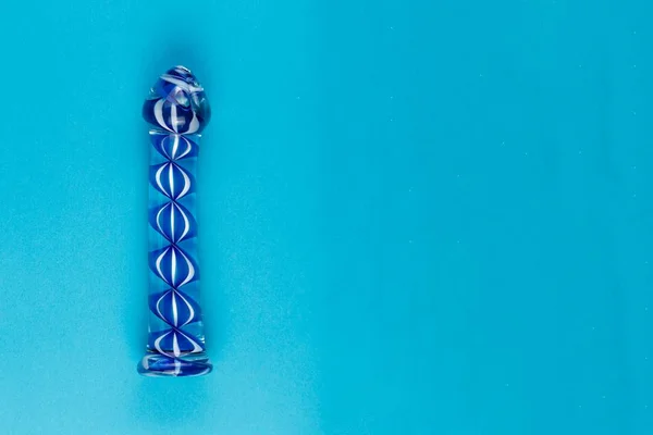 Foto colorida de um dildo de vidro transparente com azul em um fundo azul - Metrópoles