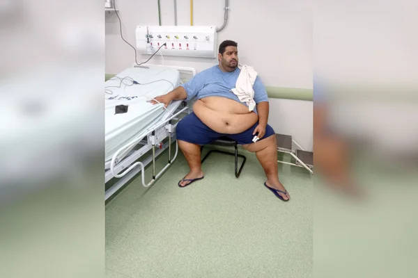 homem obeso sentado ao lado de cama de hospital