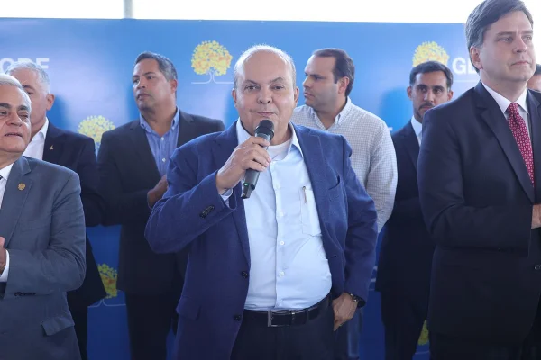 Imagem colorida de seis homens, todos vestidos de terno de cores variadas, com uma placa do GDF ao fundo