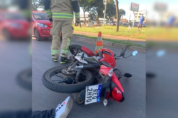 Moto vermelha caída ao chão e perna com calça jeans e tenis ao lado