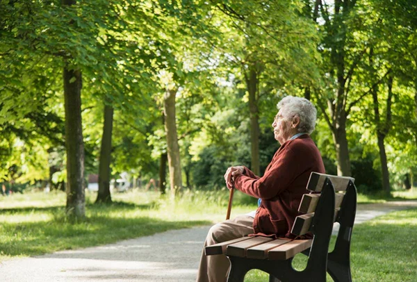 Imagem colorida: idosa solitória sentada em banco de parque com uma bengala - Metrópoles - Parkinson - alzheimer