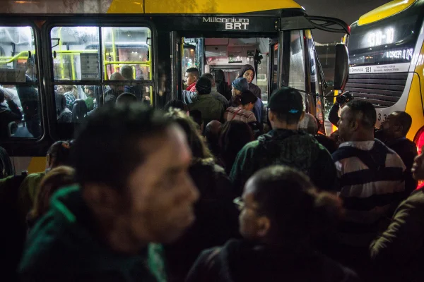 Imagem colorida mostra multidão tentado entrar em ônibus lotado durante a noite em São Paulo - Metrópoles
