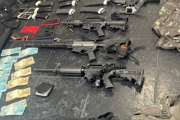 Foto colorida de arsenal apreendido pela polícia. Fuzis e notas de dinheiro aparecem no chão - Metrópoles
