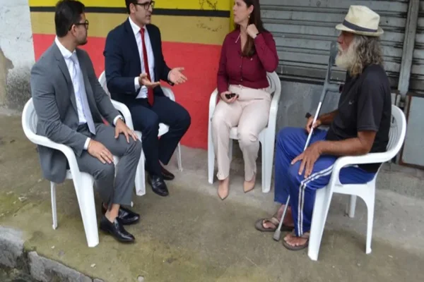 Imagem colorida mostra juiz realizando audiência com morador de rua em calçada -Metrópoles